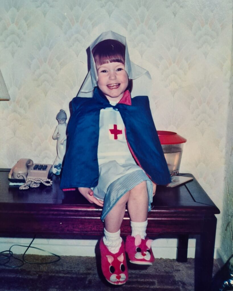 Lucy Walker, NHS Calderdale CCG Quality Manager, aged five. She is dressed in nurse dressing up outfit and smiling at the camera.